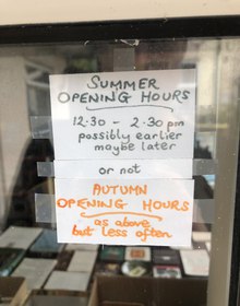 A hand-lettered sign: summer opening hours, 12.30 to 2.30, possibly earlier maybe later, or not