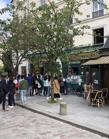 The green shopfront and its queue seen across the cobbles