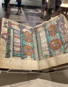 An illuminated psalter open in its case, medieval hall beyond